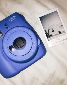 an instax camera sitting on top of a bed next to a polaroid