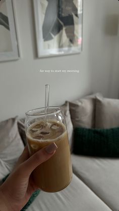 a person holding up a drink in front of a couch with pictures on the wall