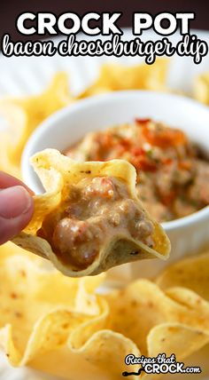 a hand holding up a tortilla chip with cheese and salsa in the background