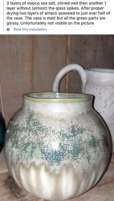 a white vase sitting on top of a wooden table next to two mugs and a tweet