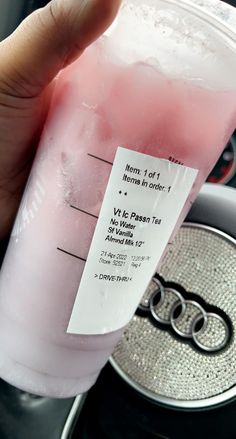 a hand holding a pink drink in front of a steering wheel with the label on it