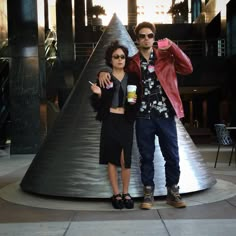 a man and woman standing next to each other in front of a cone shaped sculpture