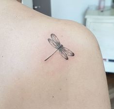 a small dragonfly tattoo on the back of a woman's shoulder