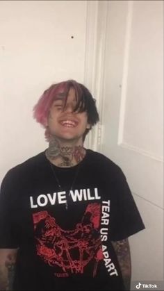 a man with pink hair and piercings wearing a black t - shirt that says love will