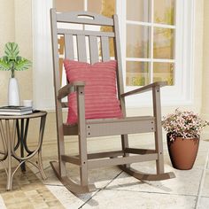 a rocking chair with a pink pillow on it next to a small table and potted plant