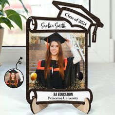 a photo frame with a graduate's cap and tassel on it, next to a potted plant