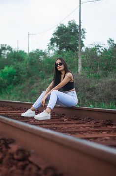 a woman sitting on train tracks with her legs crossed, wearing sunglasses and white sneakers