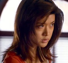 a close up of a person wearing a red shirt and looking at the camera with a serious look on her face