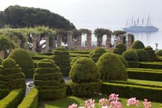 a large garden with lots of hedges in front of the water and a ship in the background