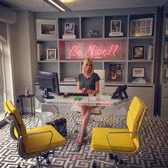 a woman sitting at a desk in an office with yellow chairs and a neon sign on the wall