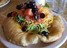 a white plate topped with a pastry covered in toppings and black olives on top of it