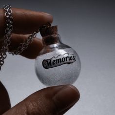 a hand holding a glass bottle with the word memories written on it and a chain attached to it