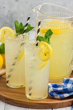 two glasses filled with lemonade sitting on top of a wooden tray