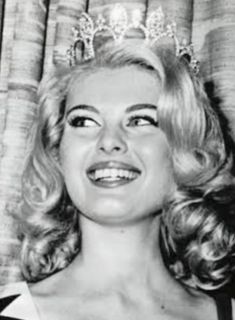 a woman wearing a tiara and smiling at the camera with her eyes closed, in front of a curtain