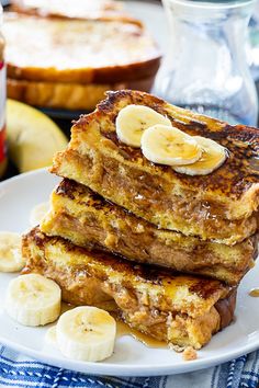 a stack of french toast with bananas and syrup on a plate next to other breakfast foods