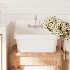 a white sink sitting on top of a wooden shelf next to a window with flowers in it