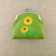 a green purse with sunflowers painted on the front and side, hanging from a wall