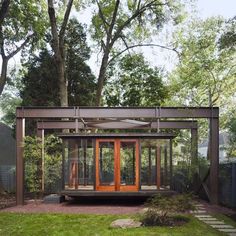 an outdoor room with wooden doors and glass windows in the middle of a grassy area