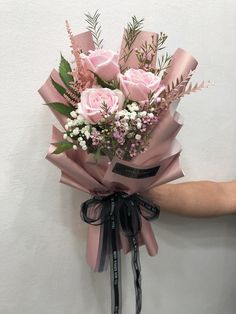 a bouquet of pink roses tied to a wall with ribbon and ribbons around it, being held by someone's hand