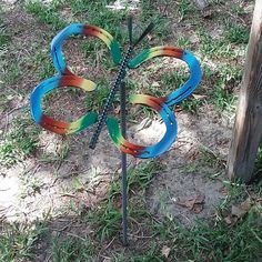 there is a colorful butterfly sculpture on the ground next to a pole and fence post