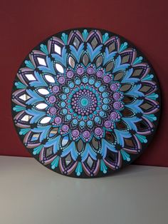 a decorative plate with blue, purple and green designs on the surface next to a red wall