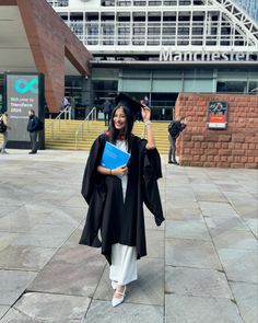 a woman wearing a graduation gown and holding a book in front of a large building