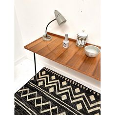 a wooden table topped with a lamp next to a black and white rug on top of a hard wood floor