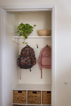 a white coat rack with two backpacks and baskets on it next to a plant