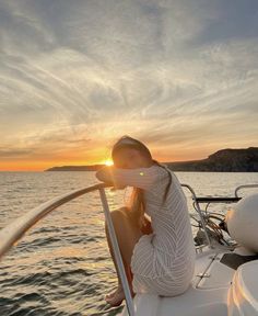 a woman sitting on the bow of a boat at sunset