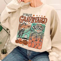 Get into the spooky spirit with our "Graveyard Smash" Sweatshirt! Featuring a retro skeleton design, this trendy fall hoodie is perfect for Halloween and the entire spooky season. With comic-style graphics and a cozy fit, it's ideal for pumpkin patches, haunted houses, or just lounging in autumnal comfort. Whether you're celebrating Halloween or just love a good ghostly vibe, this sweatshirt will keep you stylishly warm. Embrace the eerie fun and make every day a "graveyard smash" with this must-have Halloween ghost hoodie! 🔥 SAVE40: Use this code for a 40% discount when purchasing 3 or more items. I. ABOUT PRODUCT - Express your personality with our eye-catching patterns and meaningful words. Our products are comfortable, casual, and loose-fitting, making them perfect for everyday wear. Vintage Halloween Sweatshirt For Streetwear, Halloween Hoodie Sweatshirt With Graphic Print, Halloween Graphic Print Hoodie Sweatshirt, Vintage Halloween Long Sleeve Sweatshirt, Vintage Long Sleeve Halloween Sweatshirt, Fall Character Print Hoodie Sweatshirt, Retro Skeleton, Ghost Hoodie, Pumpkin Patches