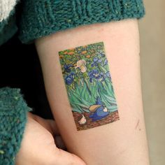 a person with a tattoo on their arm holding up a small piece of art work