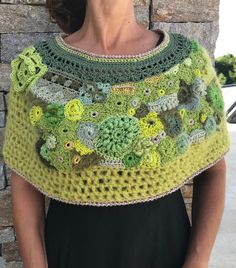 a woman standing next to a brick wall wearing a green crocheted shawl