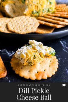 dill pickle cheese ball with crackers and crackers in the background on a black plate