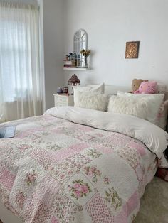 a white bed with pink and green floral bedspread in a bedroom next to a window