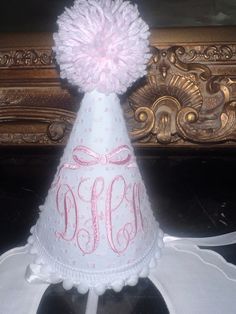 a white party hat with pink pom - poms on the top and monogrammed letters