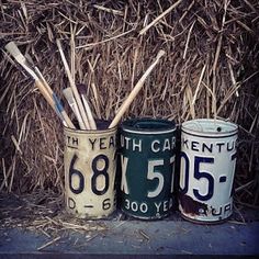 three tin cans with toothbrushes in them sitting next to some dry grass and straw