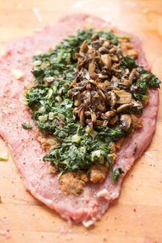 a piece of meat with spinach and mushrooms on it sitting on a cutting board