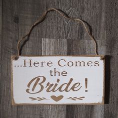 a sign that says here comes the bride hanging on a wooden wall with string attached to it