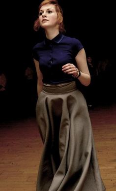 a woman is standing on a wooden floor wearing a long skirt and black shirt with blue collar