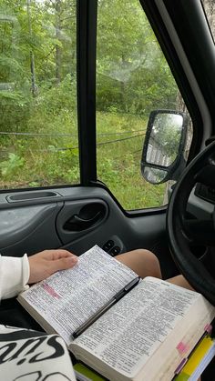 a person sitting in the driver's seat of a car holding an open book