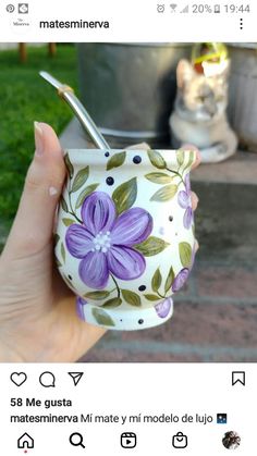 a hand holding a cup with purple flowers painted on it and a toothbrush holder