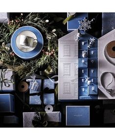 blue and silver christmas wrappings with presents around them on a black table top, surrounded by evergreen branches