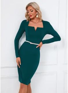 a woman in a green dress leaning against a wall with her hands on her hips