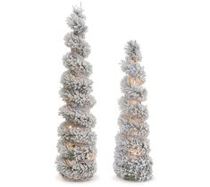 two tall white christmas trees with lights on each one and snow covered branches in the middle