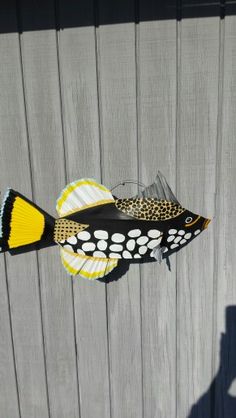 a fish made out of paper sitting on top of a wooden fence next to a person's shadow