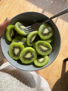 a person holding a bowl full of kiwi slices with a fork in the middle