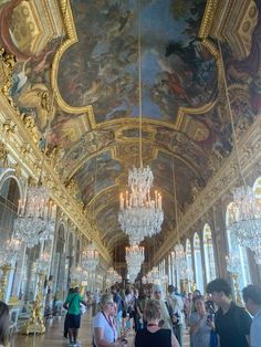 people are standing in an ornate hall with chandeliers and paintings on the walls