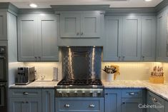 a kitchen with gray cabinets and stainless steel appliances in the center, along with marble counter tops