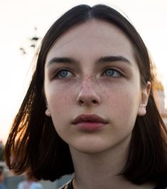 a woman with freckles on her face looking at the camera while she is outside