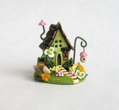 a small green house sitting on top of a lush green field with flowers and plants